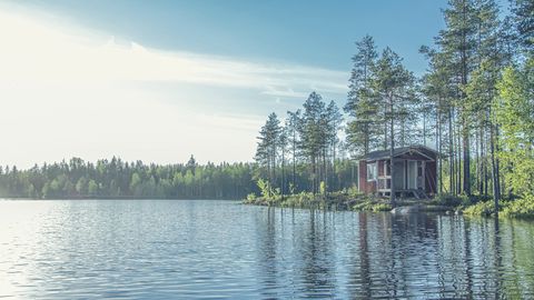 Pieni punainen sauna niemen kärjessä järven rannalla.