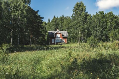 Punainen puutalo niityn takana metsän reunassa.