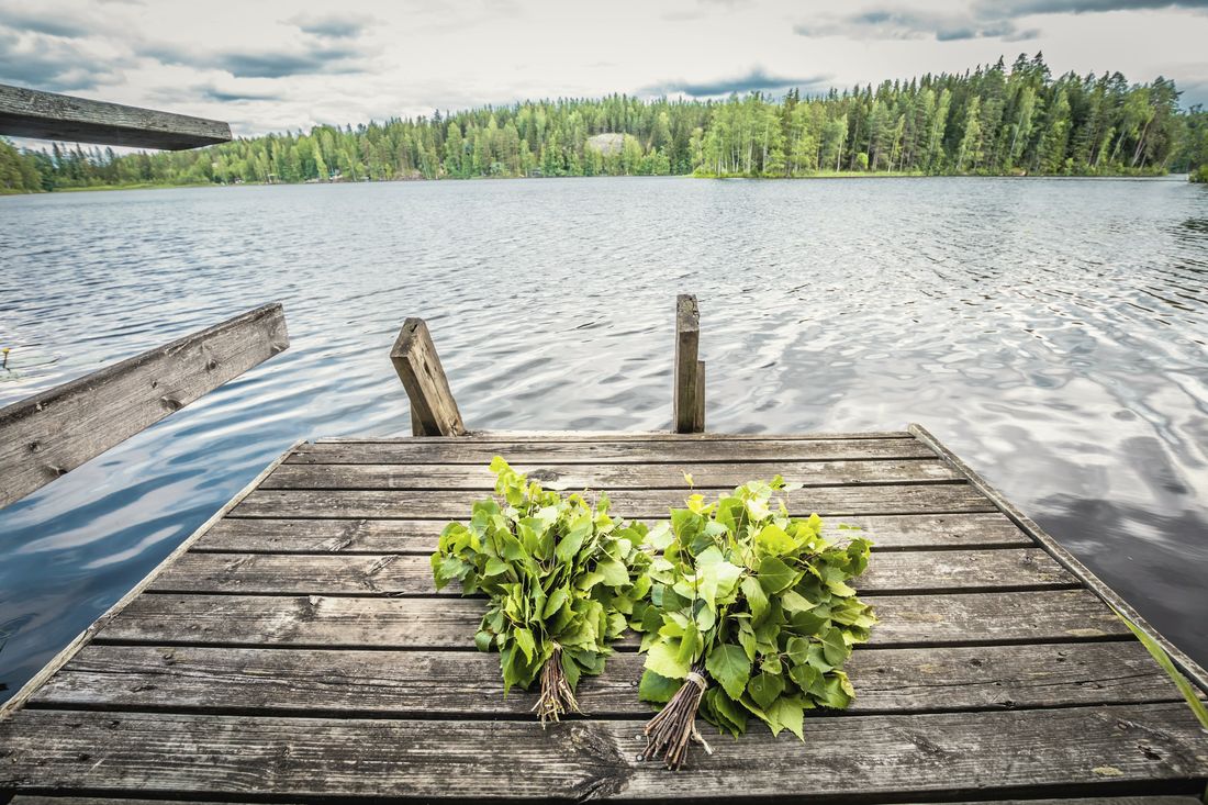 Kaksi koivuvihtaa puulaiturilla. Taustalla järvi ja metsäinen ranta.