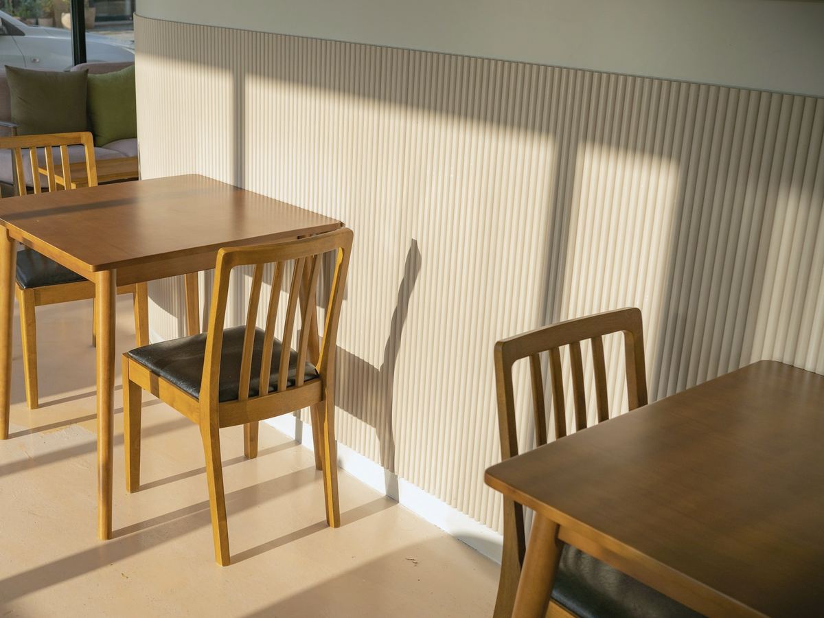 Kahvilan ikkunapöytiä ja puutuoleja iltapäivän auringossa.