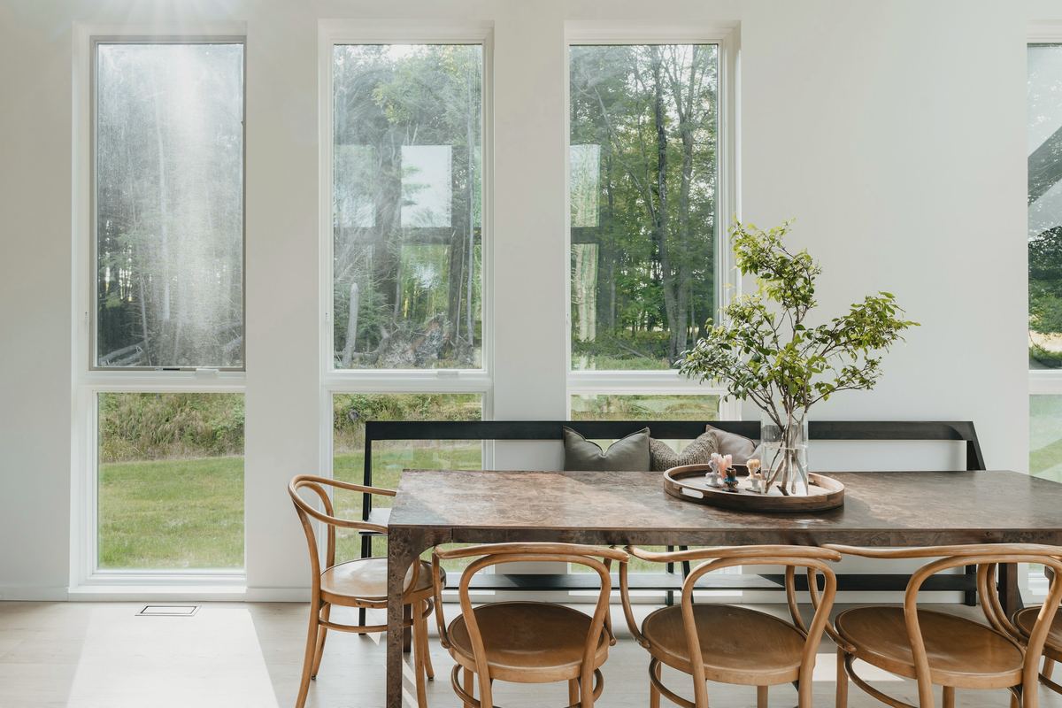 Ruokailutila, jossa on pitkä puupöytä ja lattiaan asti ulottuvat ikkunat.